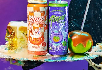 Two orange and purple cans of energy drinks next to a caramel apple and Halloween colors