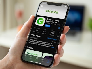 A person using a phone displaying the Groupon download page on the IOS app store.