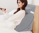 a person sitting up on a wedge pillow in a bed