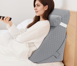 a person sitting up on a wedge pillow in a bed