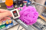 person holding the tag of a purple bath loofah in a cart