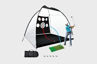 person swinging golf club in front of net
