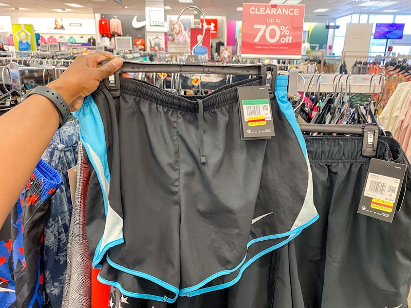 Hand holding up grey athletic shorts next to a clearance sign inside a Kohl's