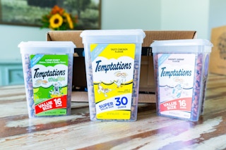 three tubs of cat treats on a hardwood floor