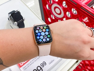 A person holding up their wrist to show their Apple watch in front of the Apple watch display and a Target shopping cart inside Target.