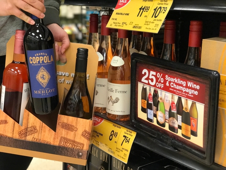 Person picking out wine bottles from a grocery store shelf.