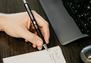 person holding a Zebra gel pen and writing a to-do list