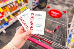 person holding 2 packs of thayers acne patches over a cart