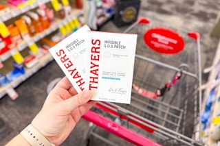 person holding 2 packs of thayers acne patches over a cart