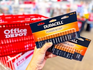 hand holding two duracell batteries packs in front of an office depot basket