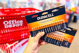 hand holding Duracell battery packs in front of an Office Depot shopping basket