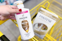 hand holding a bottle of pantene shampoo above a yellow shopping cart