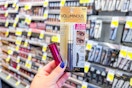 person holding loreal mascara and maybelline lipstick by the makeup display