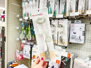 hand holding a munchkin sponge bottle brush in front of a target shelf