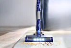 Lifestyle image of a blue PrettyCare Cordless Vacuum Cleaner (close up shot of crumbs on a carpet)
