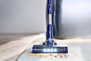 Lifestyle image of a blue PrettyCare Cordless Vacuum Cleaner (close up shot of crumbs on a carpet)