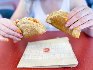 two tacos being held above the wrapper on table ng held up