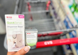 hand holding one CVS Health QuickServe dispenser base with bottle of adult multi-vitamin refill in front of shopping cart