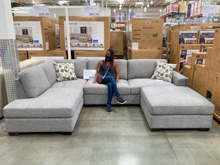 A woman sitting on a large grey sectional sofa at Costco.