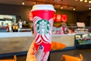 a person holding up a starbucks red cup inside of starbucks