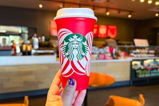 a person holding up a starbucks red cup inside of starbucks