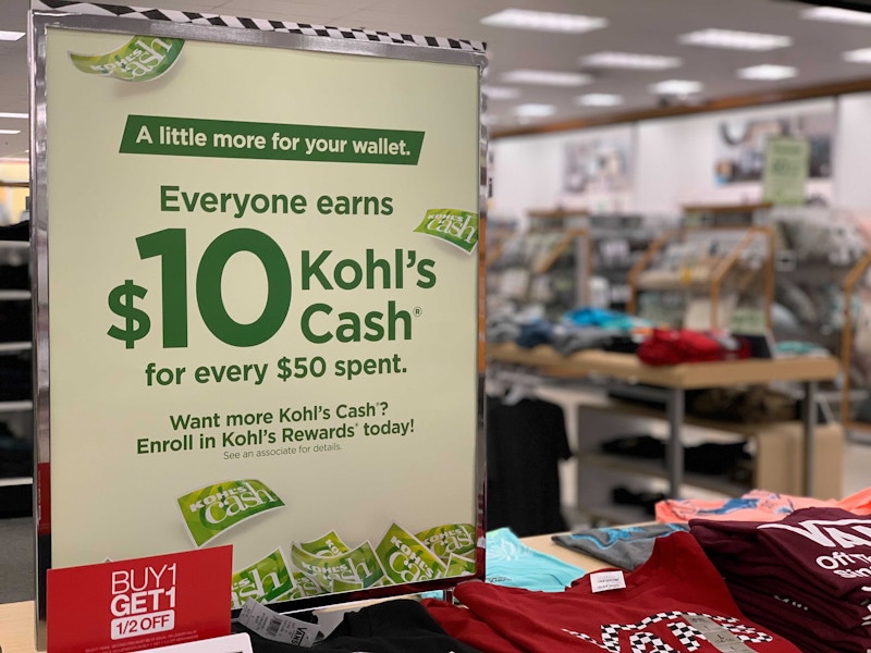 Kohls in store sign that reads Everyone earns $10 Kohls Cash for every $50 spent near a buy 1 get one ½ off sign on a tee shirt display s...