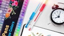 colorful gel pens on a table with a clock