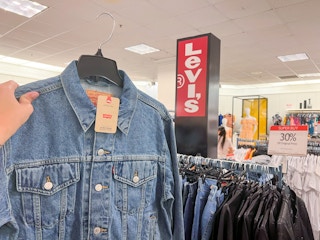 a person holding a levi's ex boyfriend denim trucker jacket with a levi's sign and a 30 percent off sale sign in the background