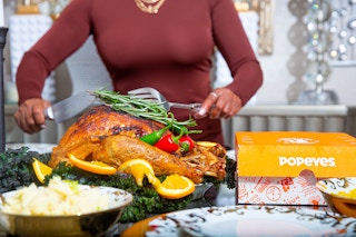 Person in a brown dress cutting a turkey next to an orange Popeyes box