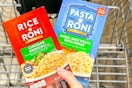 hand holding boxes of rice a roni pasta roni over shopping cart
