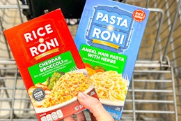 hand holding boxes of rice a roni pasta roni over shopping cart