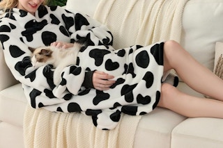 a woman wearing a blanket and cuddling a cat