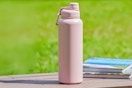Lifestyle image of the Mainstays 40 oz Pearl Blush Pink Insulated Stainless Steel Water Bottle on a table outdoors