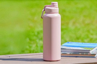 Lifestyle image of the Mainstays 40 oz Pearl Blush Pink Insulated Stainless Steel Water Bottle on a table outdoors