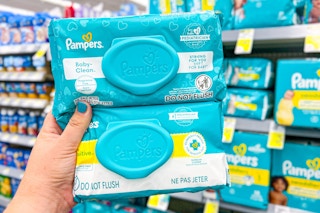 hand holding two packs of pampers baby wipes in a store aisle