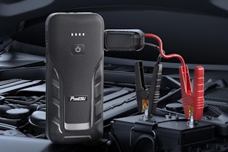 A black jump starter has a black and a red clamp clamped on to the battery in an unusually clean car.