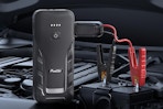 A black jump starter has a black and a red clamp clamped on to the battery in an unusually clean car.