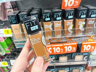 A hand holding Maybelline fit me foundation in a store