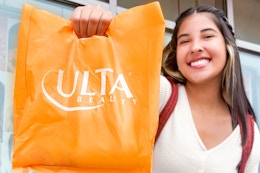 a woman holding out an ulta shopping bag outside an ulta store