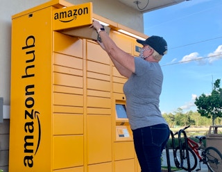 A woman taking an Amazon package out of an Amazon hub locker.
