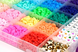 A clear plastic box has many compartments, each full of a different color or kind of bead, e.g. clay, polymer, heishi, shiny stars, letters.