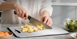 a person chopping potatoes on a titanium cutting board