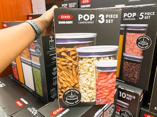 someone grabbing a box of oxo food storage containers on a display of other containers in macys