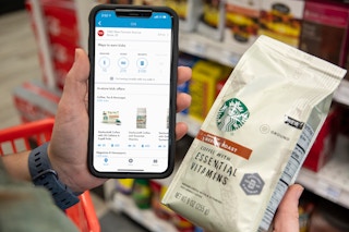 A person holding a bag of starbucks coffee next to a cell phone with the shopkick app on it.