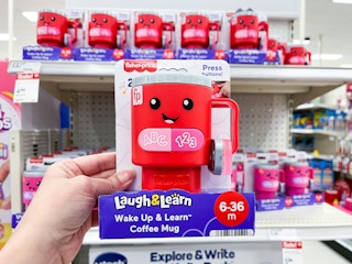 hand holding a fisher price coffee mug in front of a target shelf