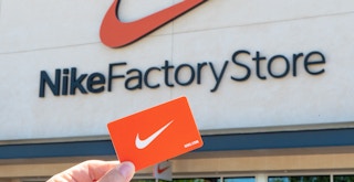 Someone holding up a Nike card in front of a Nike Factory Store