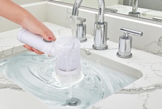 a hand holding a spin scrubber in a sink