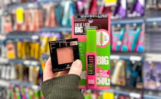A person's hand holding up some Maybelline Fit Me blush and some Great Lash BIG mascara in front of a wall of makeup in an aisle at CVS
