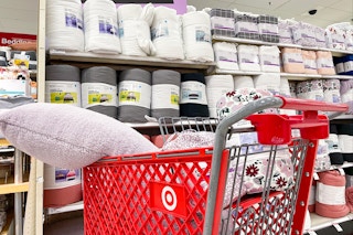 A Target shopping cart filled with bedding items parked in front of a shelf in the College Shop section in Target.