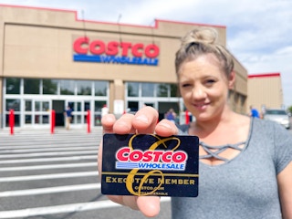 woman holding costco membership card in front of costco store
